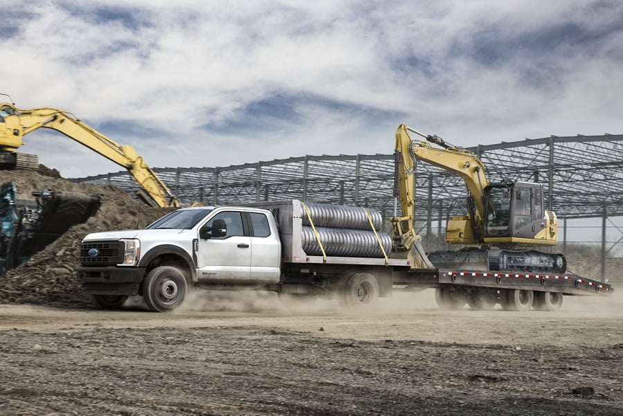 2025 Ford Super Duty® F-350® loaded with pipes and pulling a trailer with a backhoe