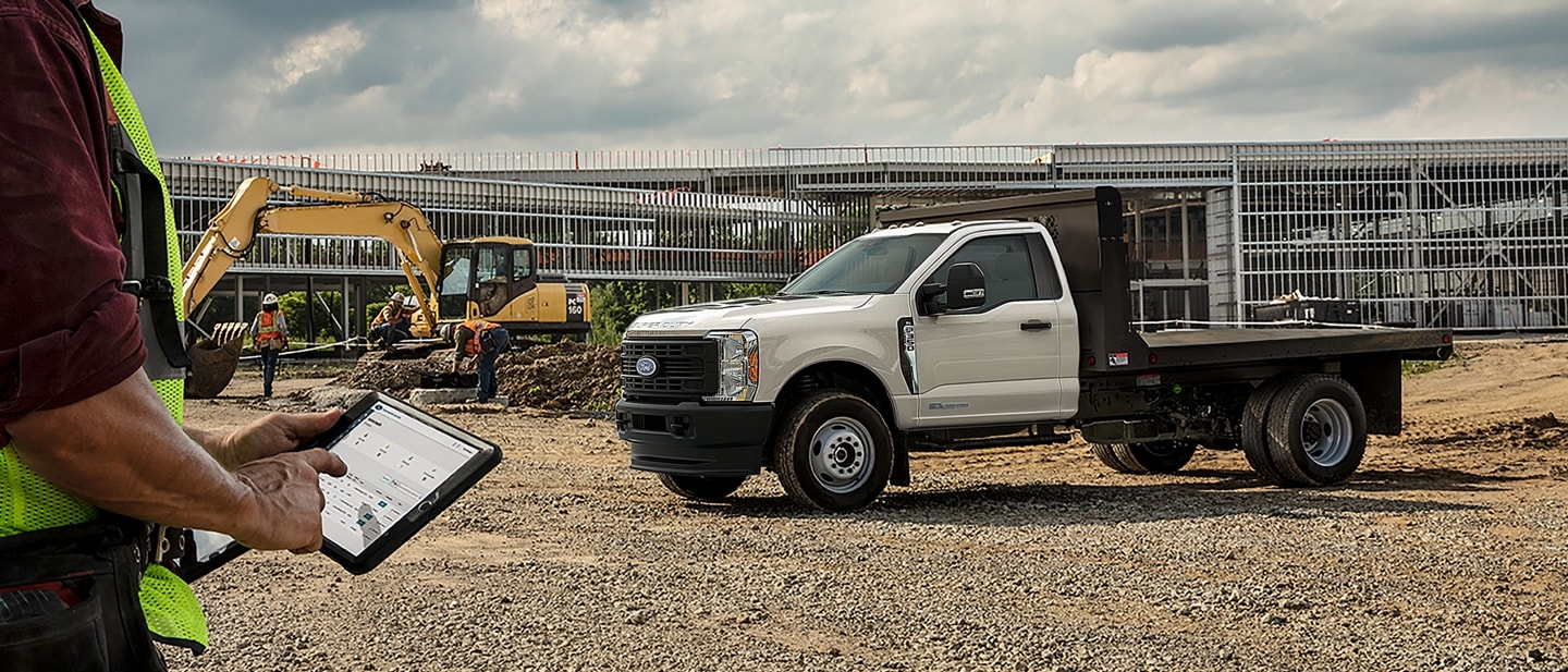A 2025 Ford Super Duty® F-350® XL flatbed at a jobsite as a worker operates a tablet