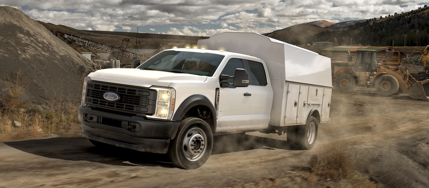 2025 Ford Super Duty® F-450® XL with a utility box driving up a dirt road job site