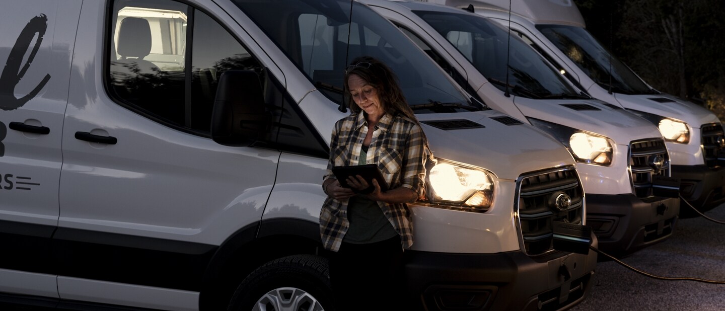 A woman standing outside next to a fleet of 2023 Ford E-Transit™ vehicles