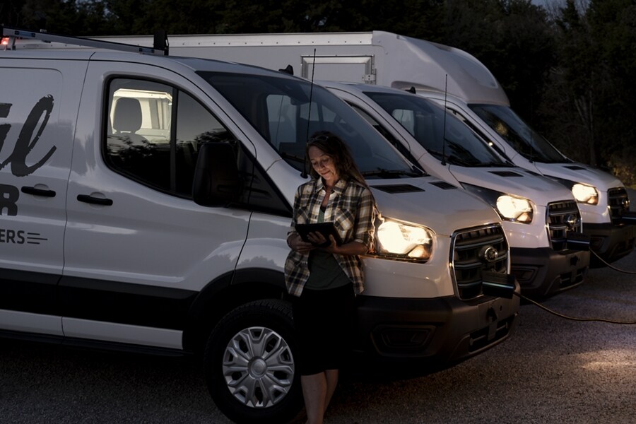 Woman leans against a 2023 Ford E-Transit™ van with a tablet in her hand