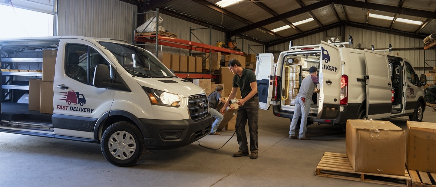 Two 2023 Ford E-Transit™ vans in a warehouse, one being charged, one being loaded