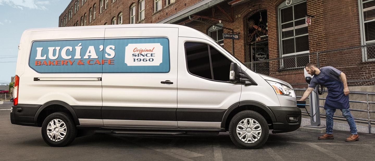 2023 Ford E-Transit™ van parked in front of a business as a man attaches the plug