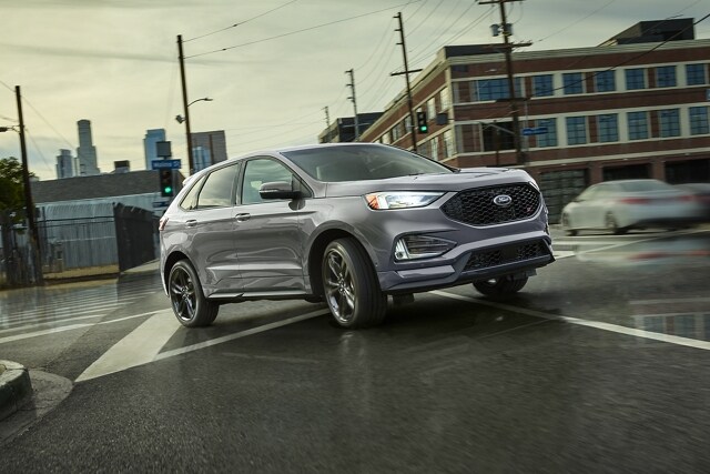 A 2023 Ford Edge® ST SUV in Iconic Silver being driven on a wet city road