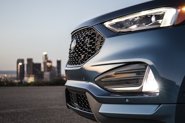 Close-up of LED headlamps and fog lamps with city skyline in the background