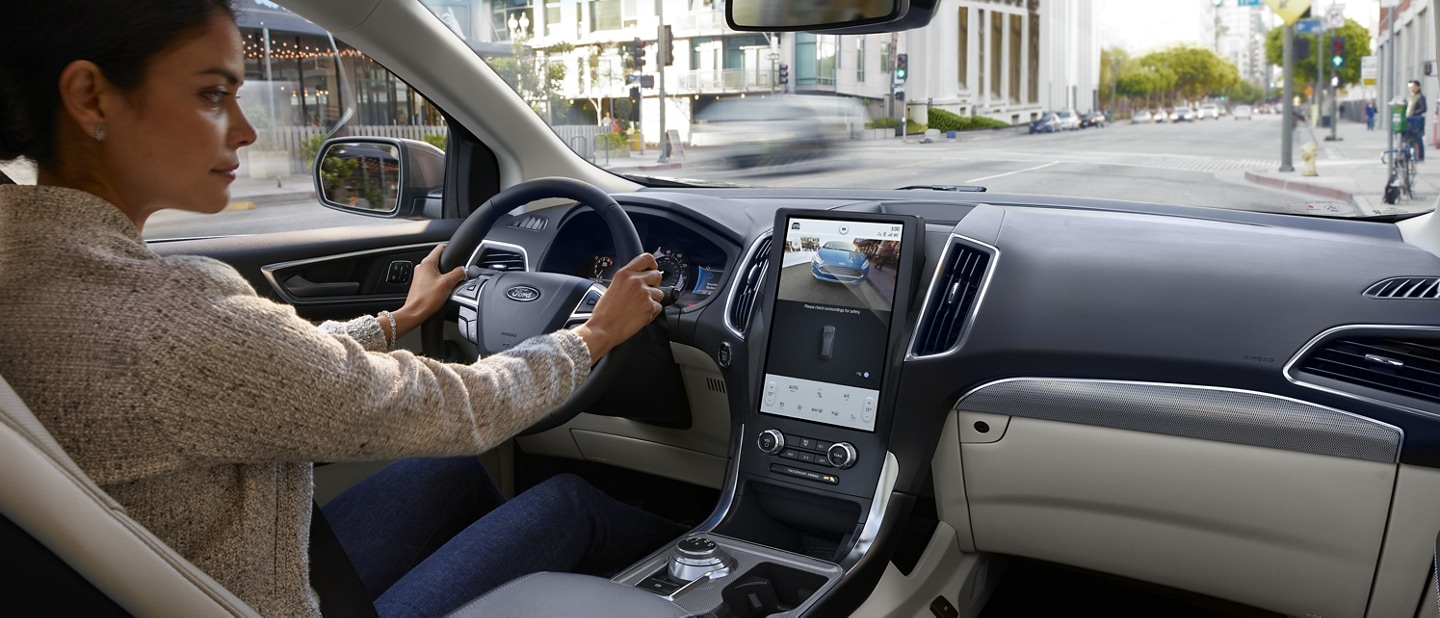 Interior view of a 2024 Ford Edge® centre console as a woman driving glances at touchscreen