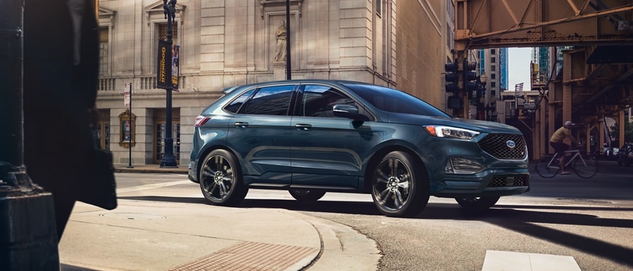 2024 Ford Edge® ST model in Stone Blue driving around a curve in a city