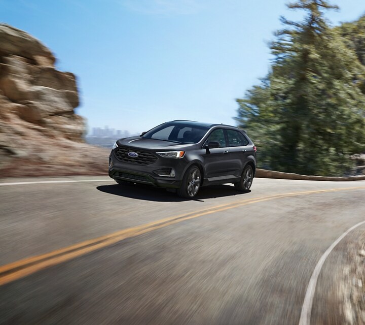 2024 Ford Edge® SUV in Carbonized Grey driving on a road overlooking a city