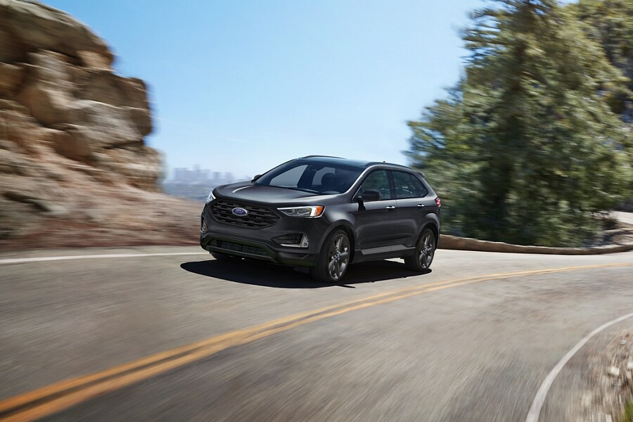 2024 Ford Edge® SEL in Carbonized Grey being driven on a curvy road with city in background