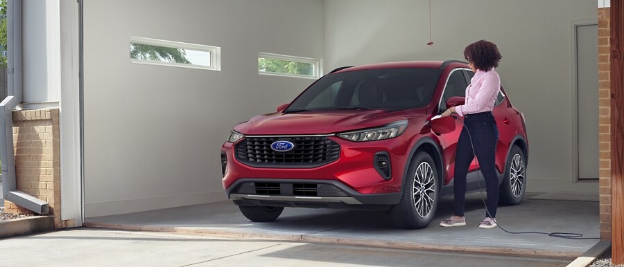 Person in a garage charging a 2023 Ford Escape® Plug-in Hybrid in Rapid Red Metallic Tinted Clearcoat
