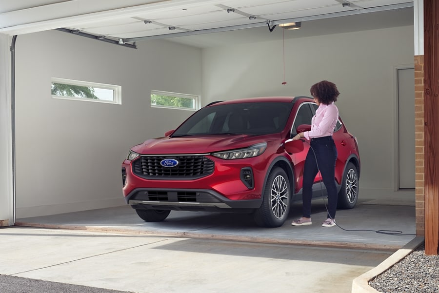 Person in a garage charging a 2023 Ford Escape® Plug-in Hybrid in Rapid Red Metallic Tinted Clearcoat