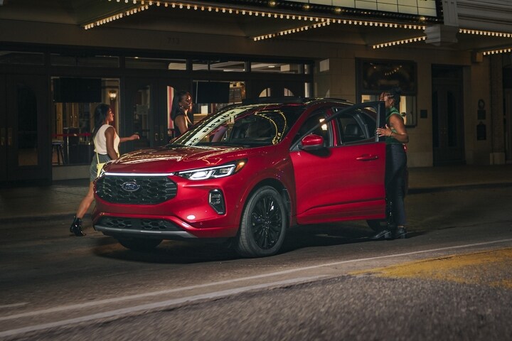 A 2023 Ford Escape® at night parked in front of a theatre woman getting in