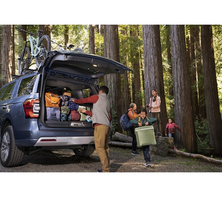 A family unloading gear from a 2023 Ford Expedition SUV parked in the woods