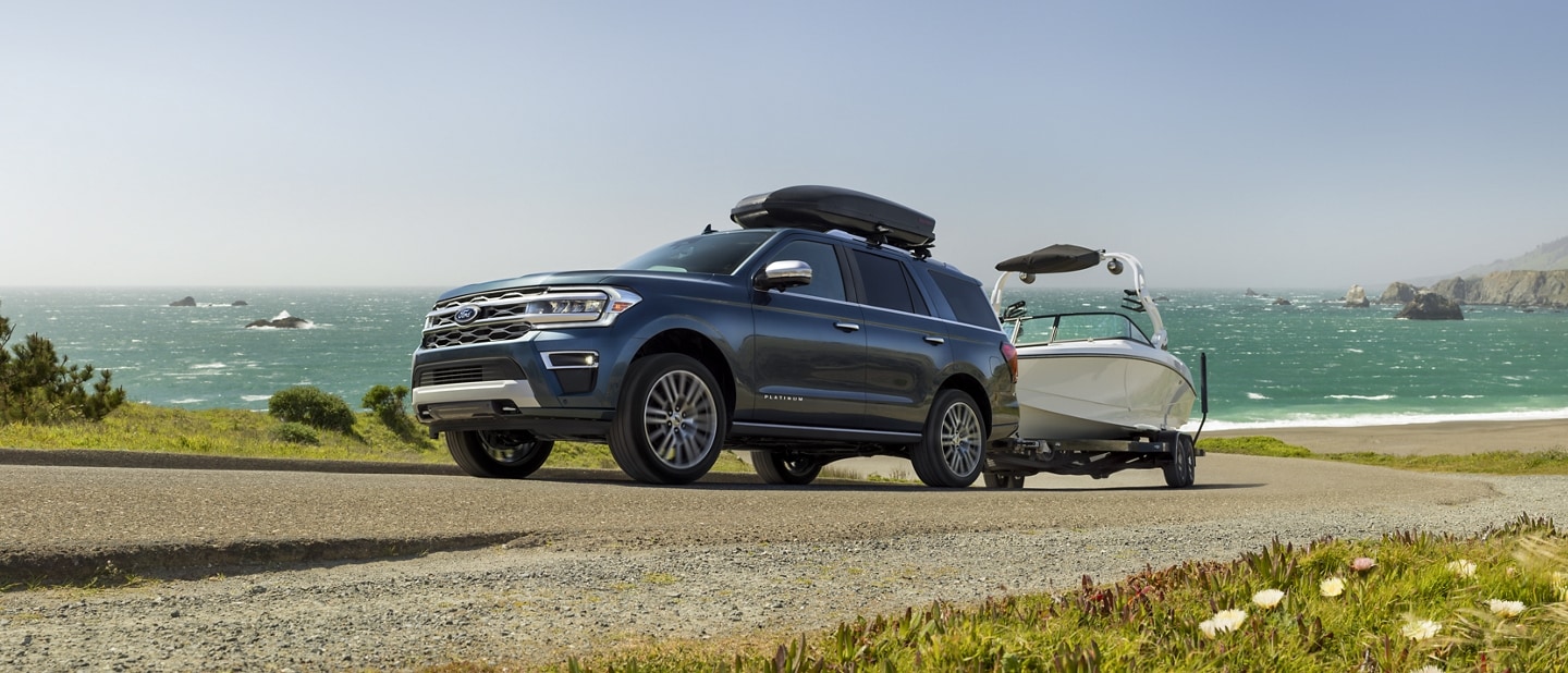 A 2023 Ford Expedition SUV towing a boat up a bill with water in background