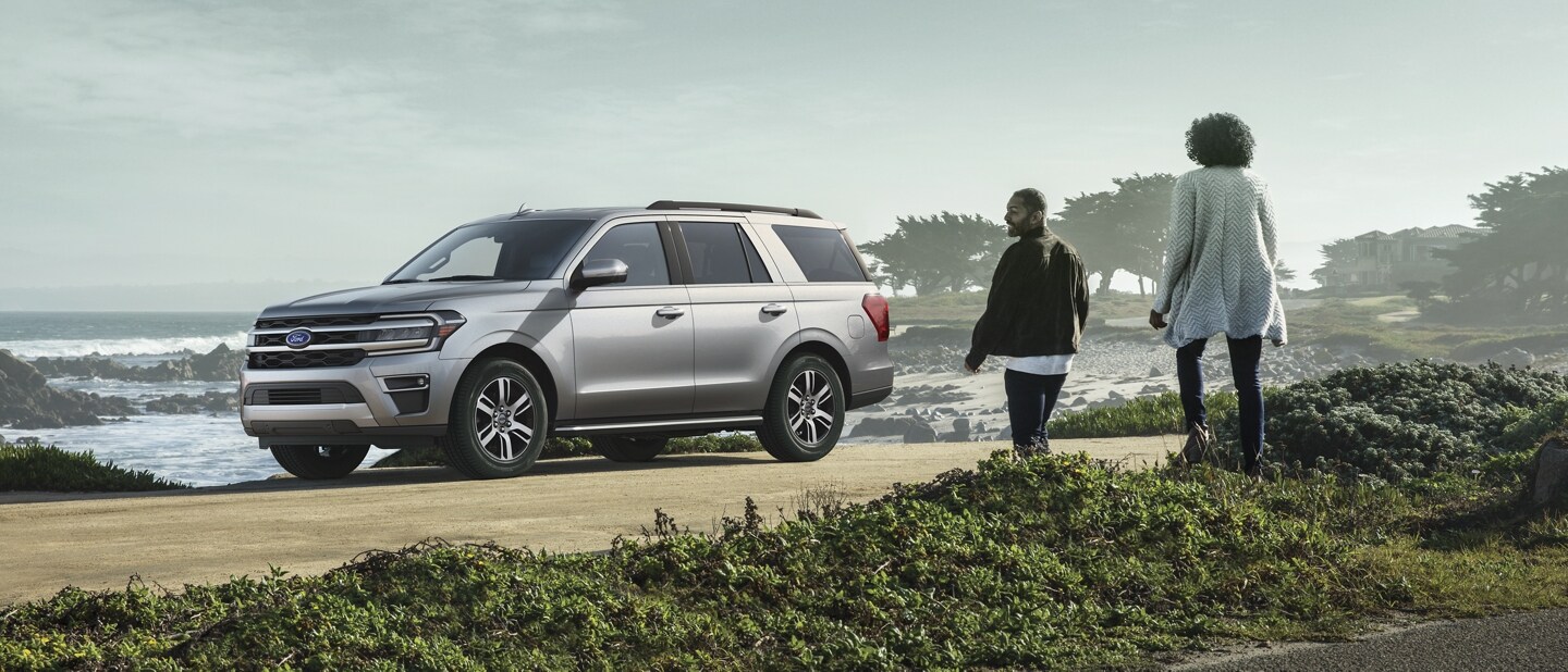 Two people approach a 2023 Ford Expedition SUV parked next to a body of water