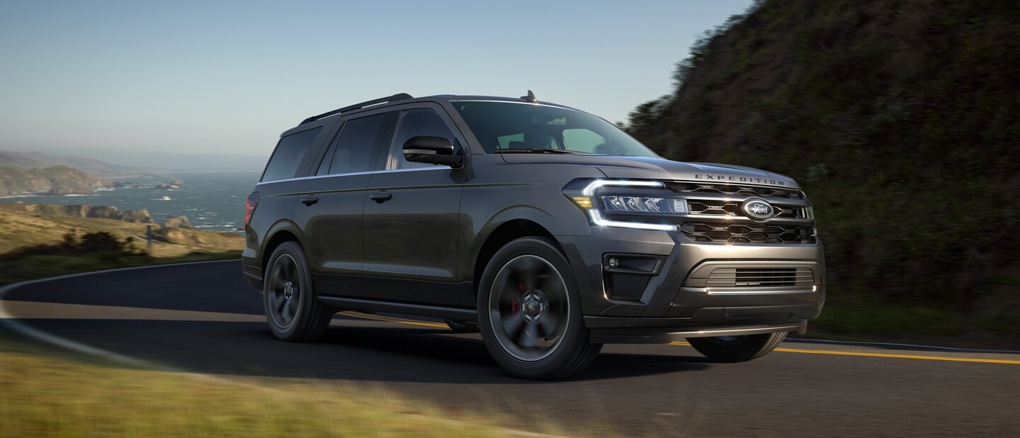 A 2023 Ford Expedition SUV being driven on a mountain road with a body of water in the background
