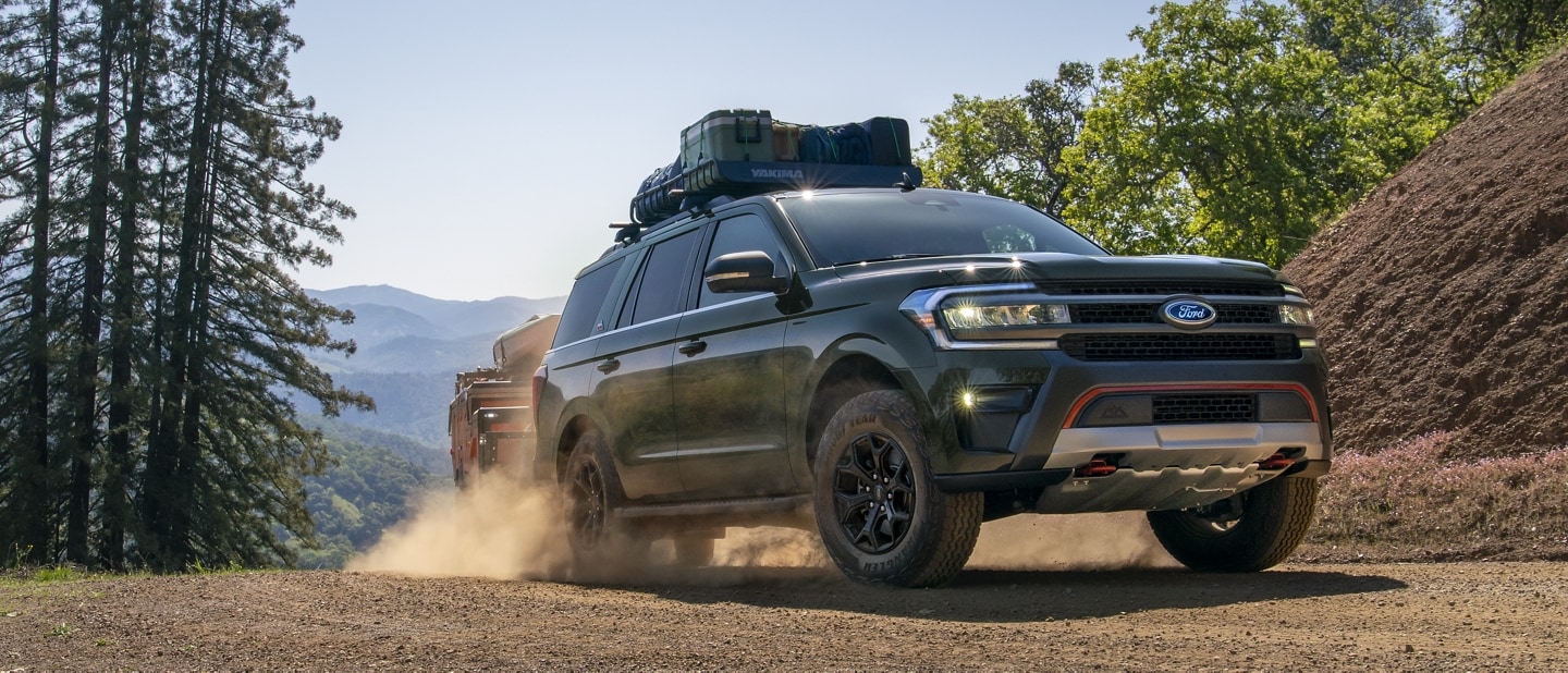 A 2024 Ford Expedition® Timberline model being driven on a mountain road towing a trailer