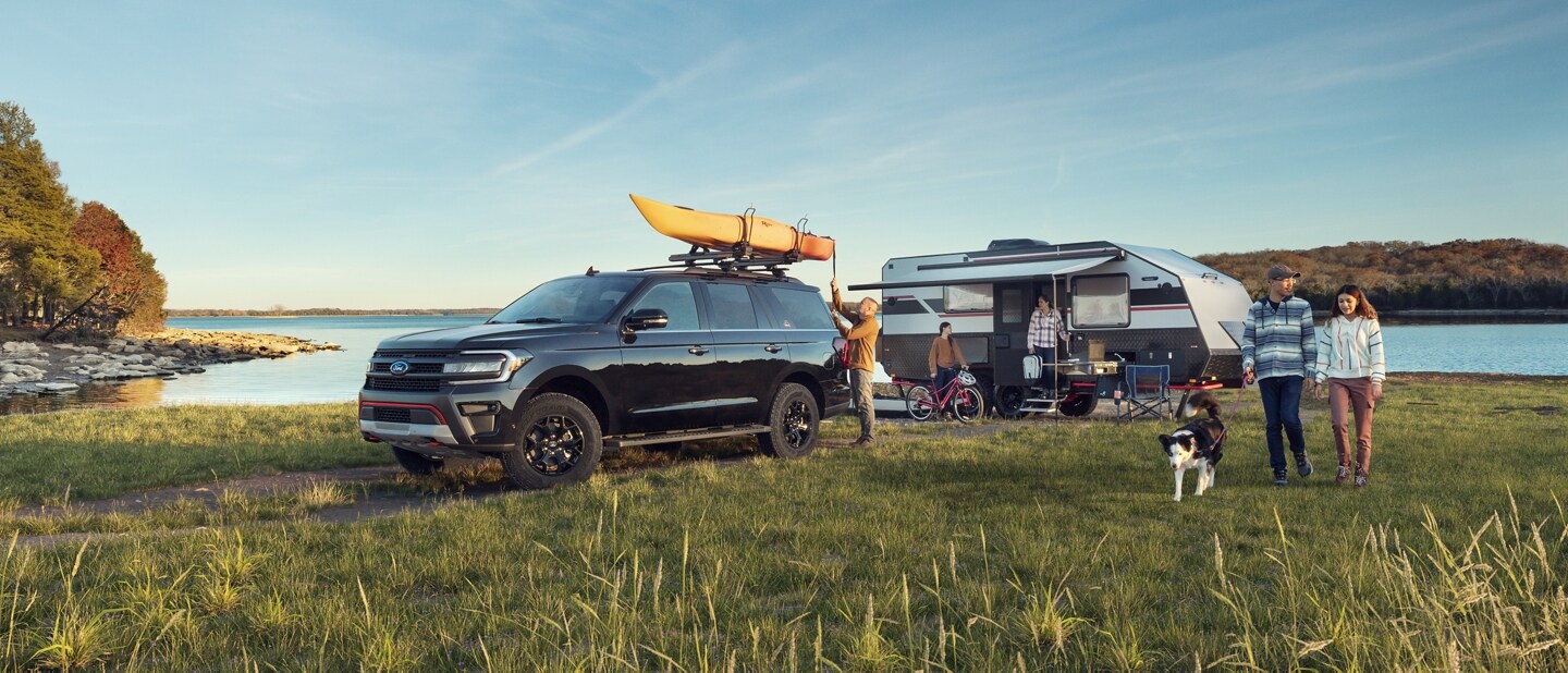 A 2024 Ford Expedition® Timberline® parked by a lake with a family and camper in background