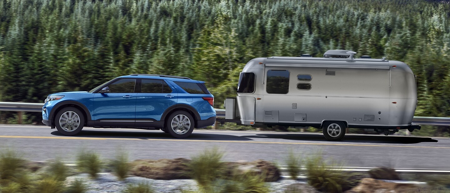 2023 Ford Explorer® Hybrid SUV towing a camper on a forest road