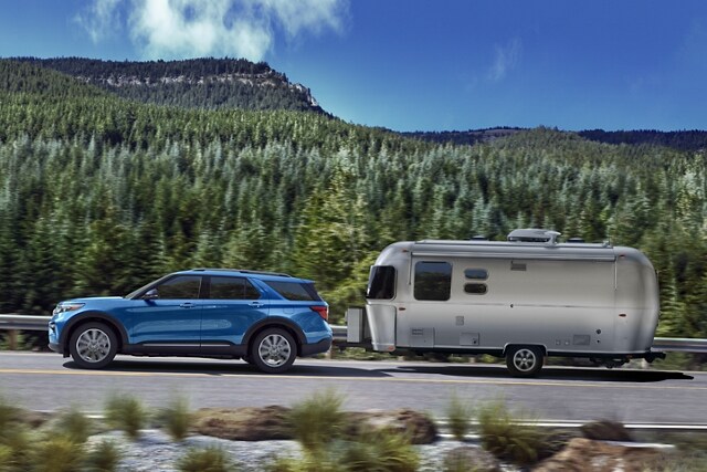 2023 Ford Explorer® Hybrid SUV towing a camper on a forest road