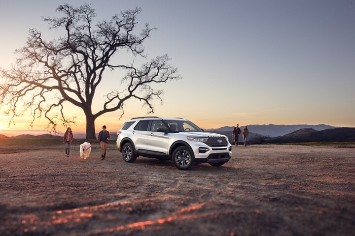 2023 Ford Explorer® XLT model with XLT Sport Appearance Package parked under a tree with a family nearby