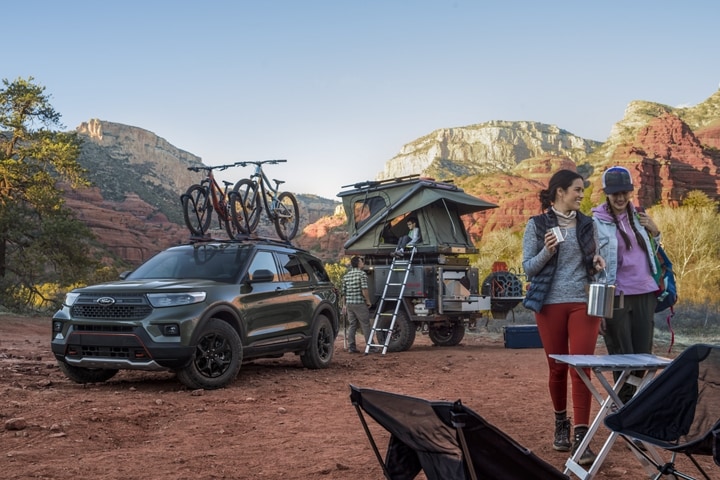 2023 Ford Explorer® Timberline® SUV in Forged Green Metallic parked in the desert with a trailer-top tent and family