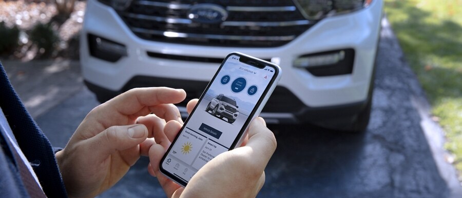 Person standing in front of a 2023 Ford Explorer® SUV holding a smartphone displaying the FordPass™ App