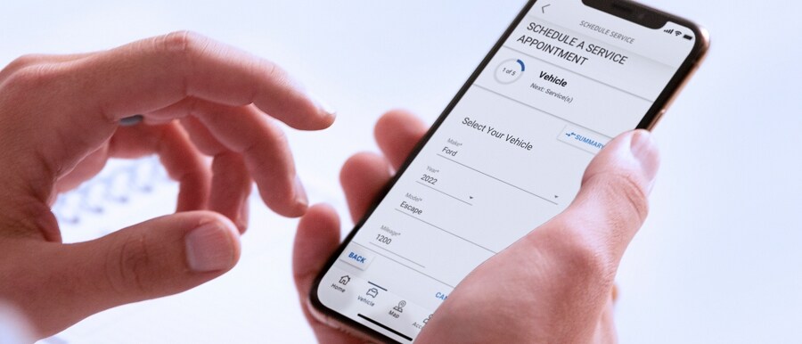 A hand holds a smartphone displaying the FordPass™ App