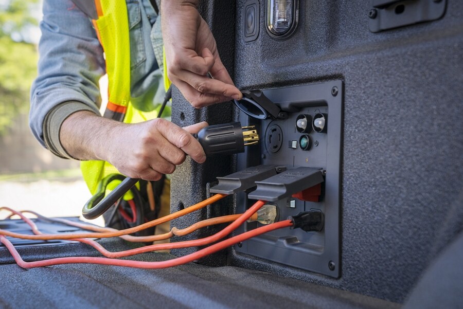 Close up of a person plugging a cord into the pro power onboard outlet in the bed of a 2021 Ford F 1 50