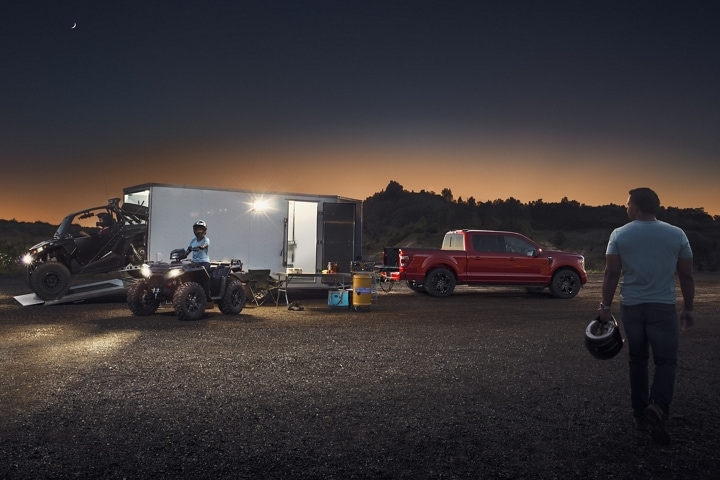 A boy riding an ATV and a 2023 Ford F-150® LARIAT® parked hitched a trailer