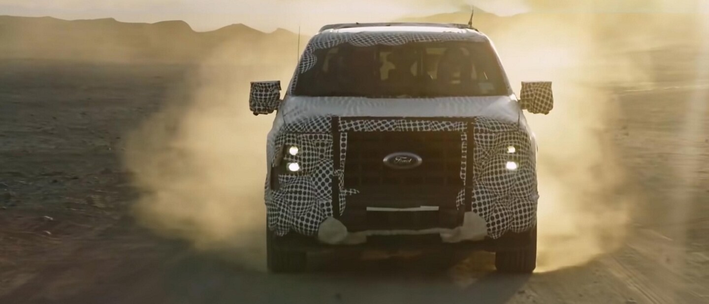 Front view of a disguised 2023 Ford F-150® PowerBoost™ hybrid being driven off-road in the desert
