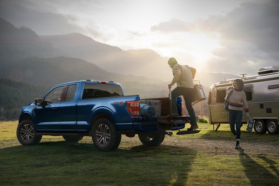Man using the liftgate step on a 2023 Ford F-150® XL Super Cab pickup in Atlas Blue at a campground