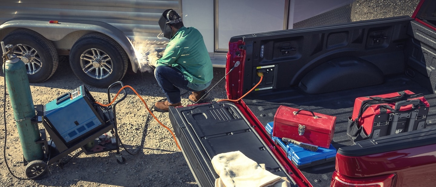 Person welding a trailer near a 2023 Ford F-150® while using the Pro Power Onboard feature