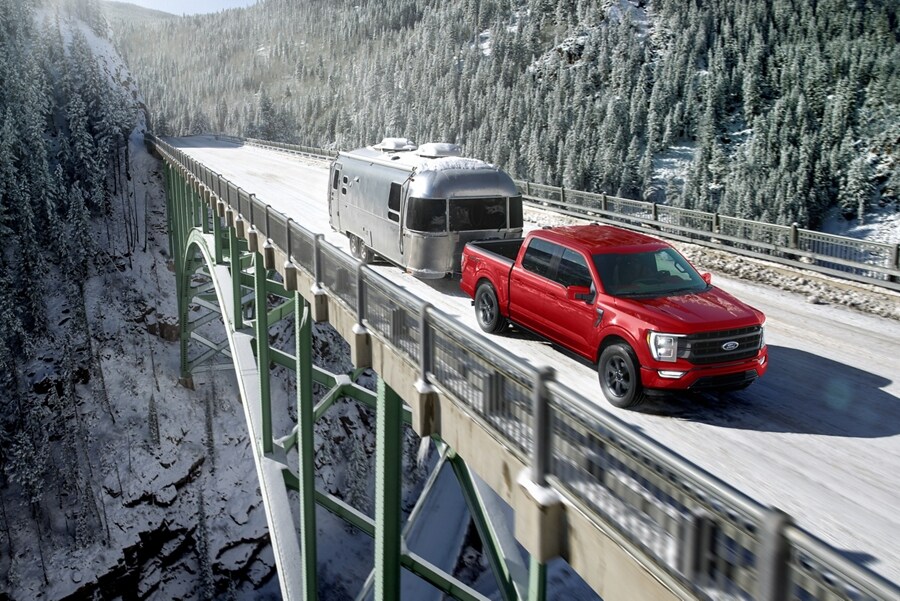 2023 Ford F-150® LARIAT® in Rapid Red pulling an airstream camper over a suspension bridge