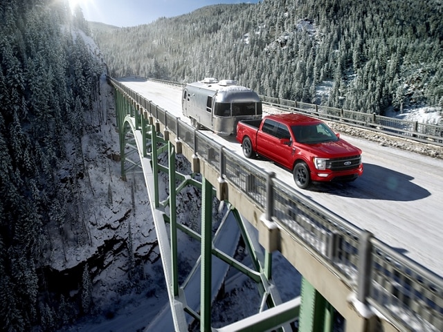 2023 Ford F-150® LARIAT® in Rapid Red pulling an airstream camper over a suspension bridge