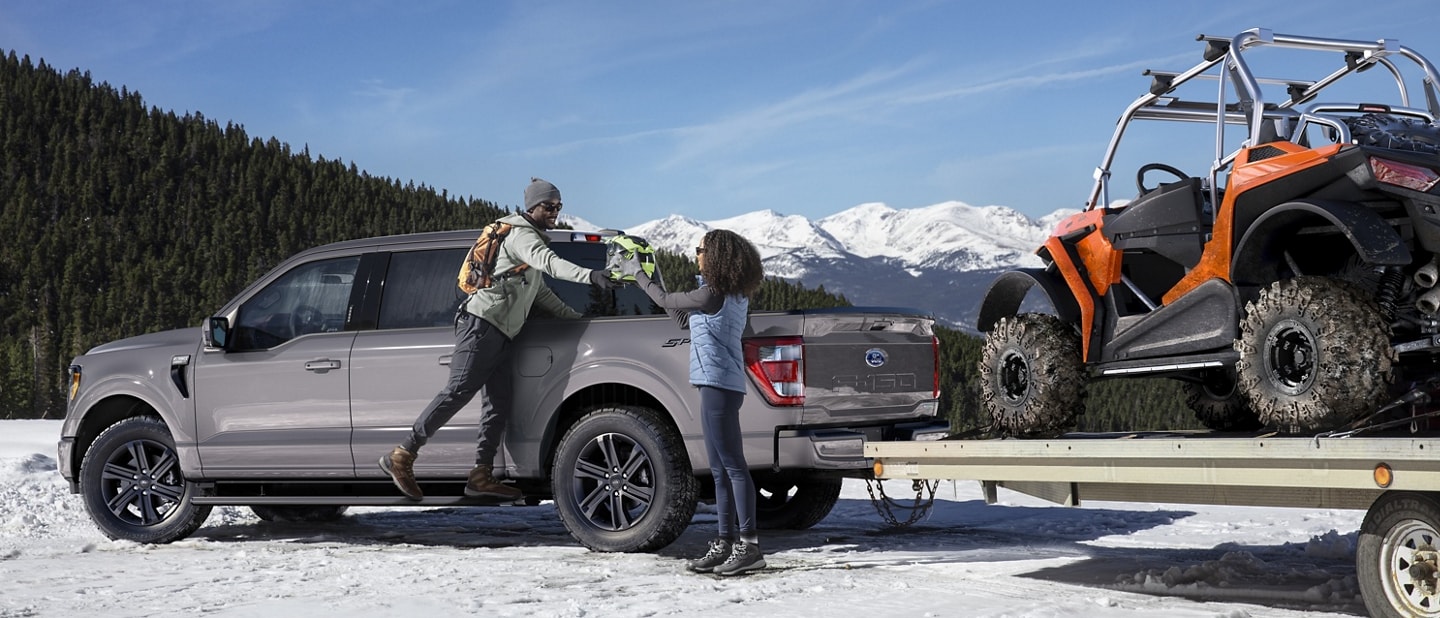 Man and woman unloading gear from the back of a 2023 Ford F-150® LARIAT® hitched to a trailer carrying an ATV