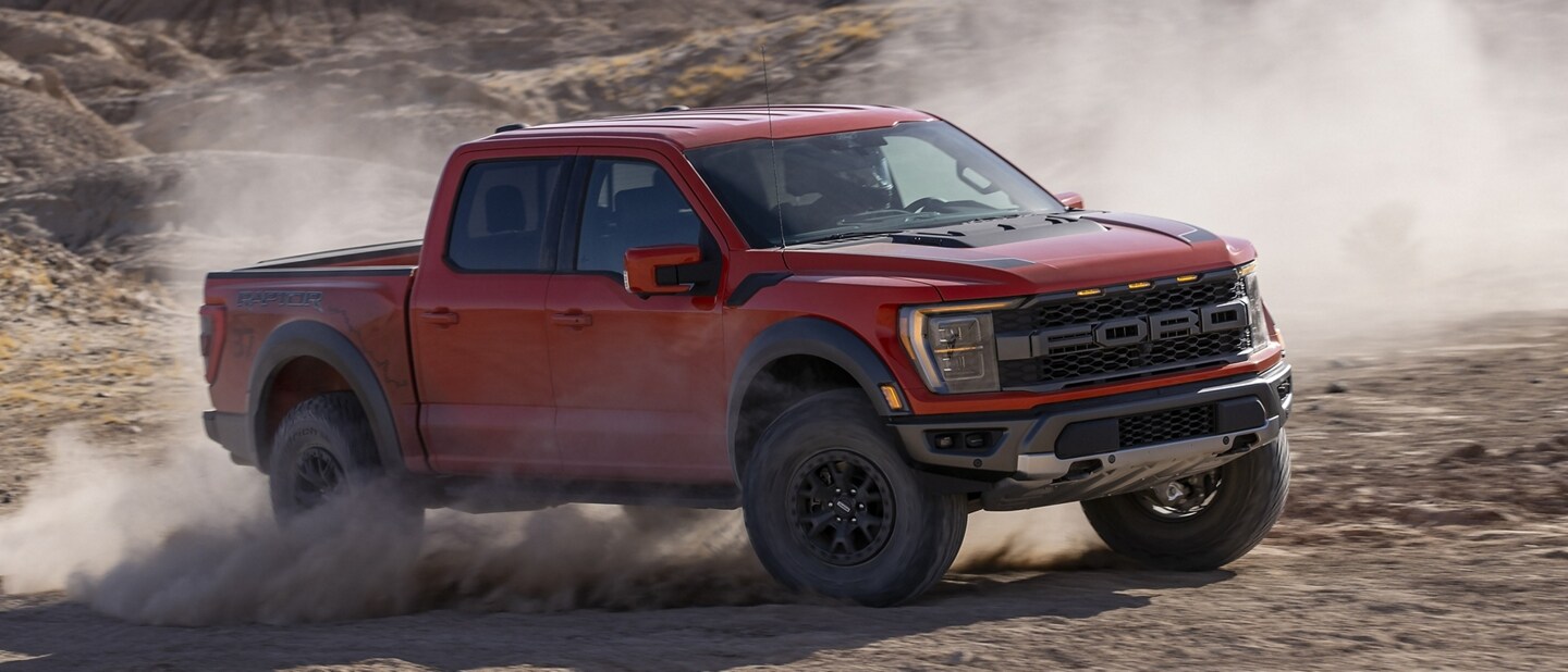 A 2023 F-150® Raptor® being driven in the desert kicking up dust