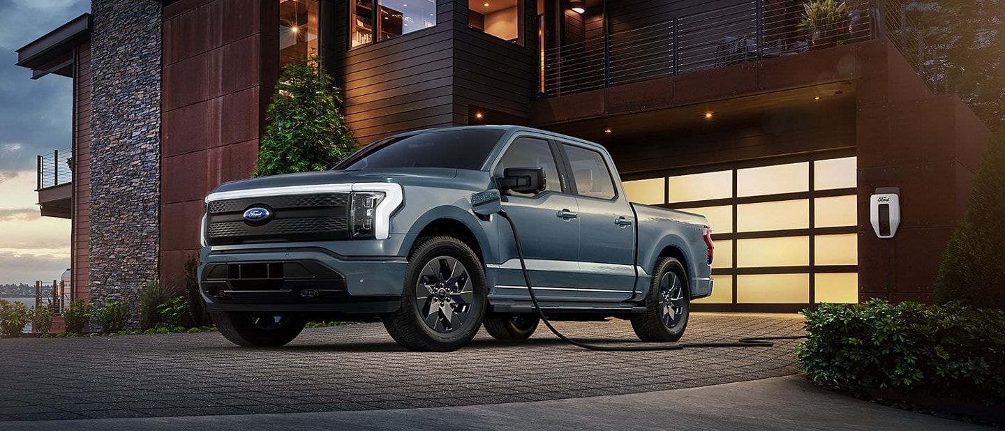 2023 Ford F-150® Lightning® pickup in Atlas Blue parked in front of a modern home hooked up to a home charger