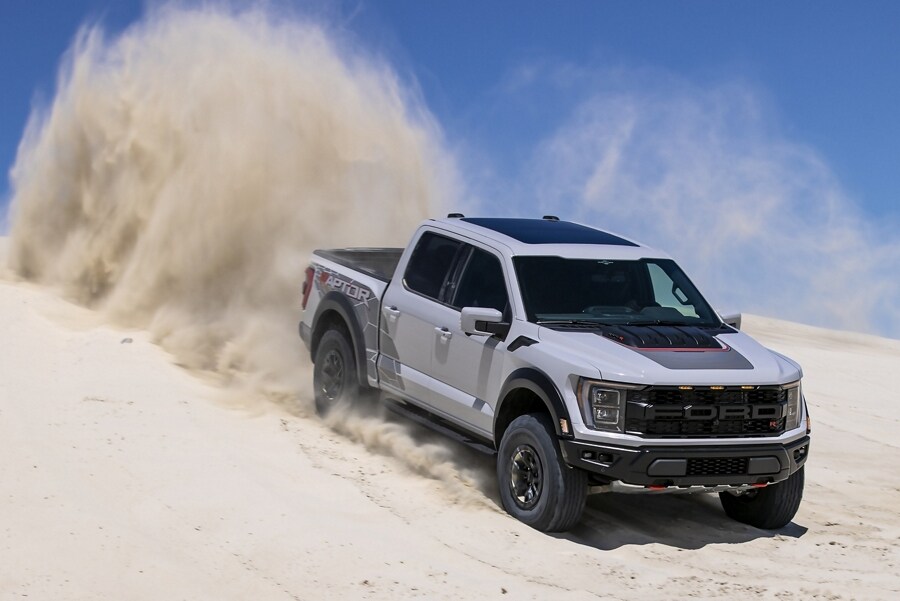 A 2023 Ford F-150® Raptor® R truck in Avalanche Grey being driven down a sloped dirt road kicking up dust
