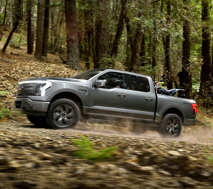 A 2023 Ford F-150® Lightning® being driven through a forest on a dirt road