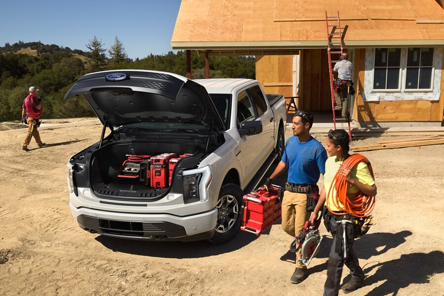 2023 Ford F-150® Lightning® parked with front trunk open on a worksite and two workers carrying gear