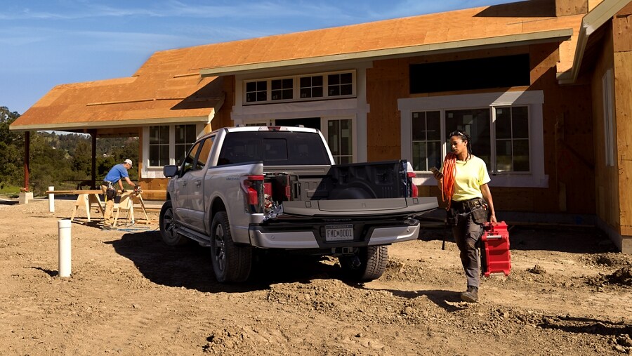 Construction worker carrying equipment with the 2023 Ford F-150® Lightning® tailgate open