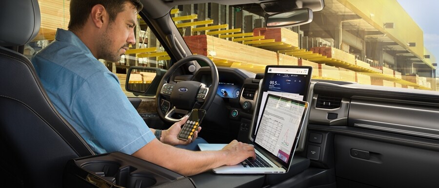 Man working on his laptop inside a 2023 Ford F-150® Lightning® parked at a lumber yard