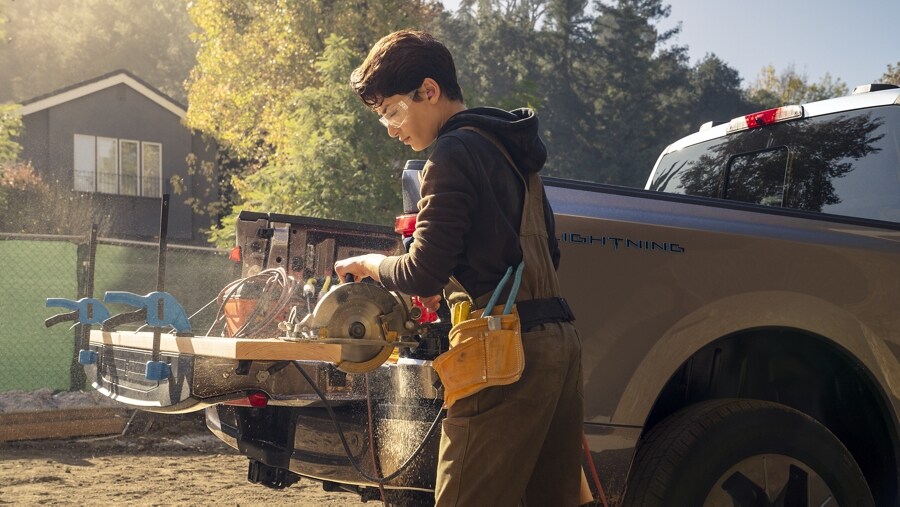 A worker using the flat work surface of the tailgate to cut a board on job site
