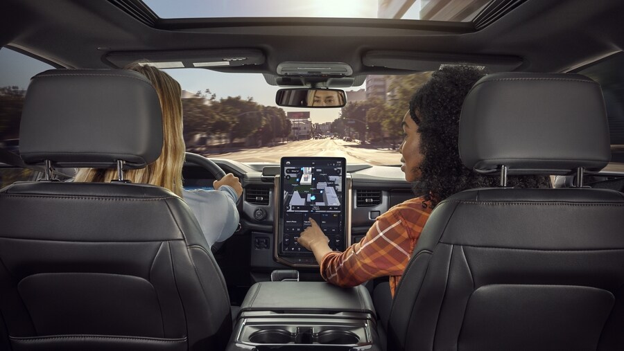 View from rear seat of 2023 Ford F-150® Lightning® with woman passenger pointing on touchscreen map