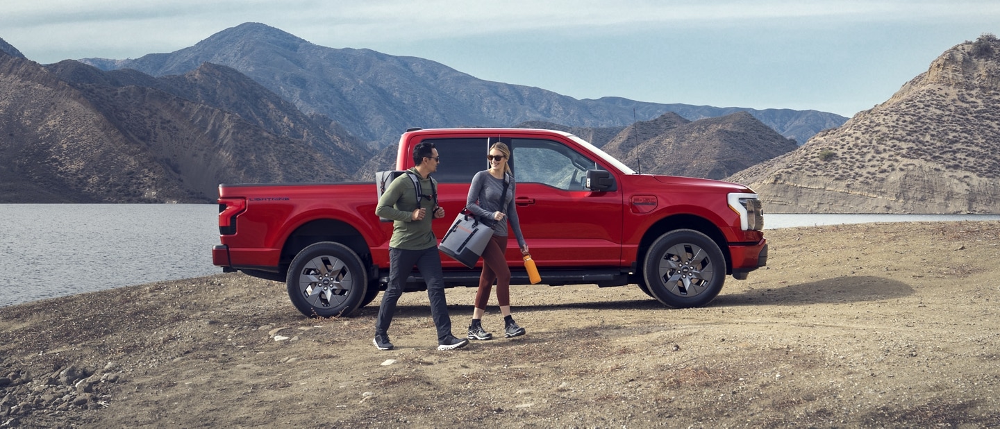 A couple walking near a 2023 Ford F-150® Lightning® parked near a lake with mountains in the background