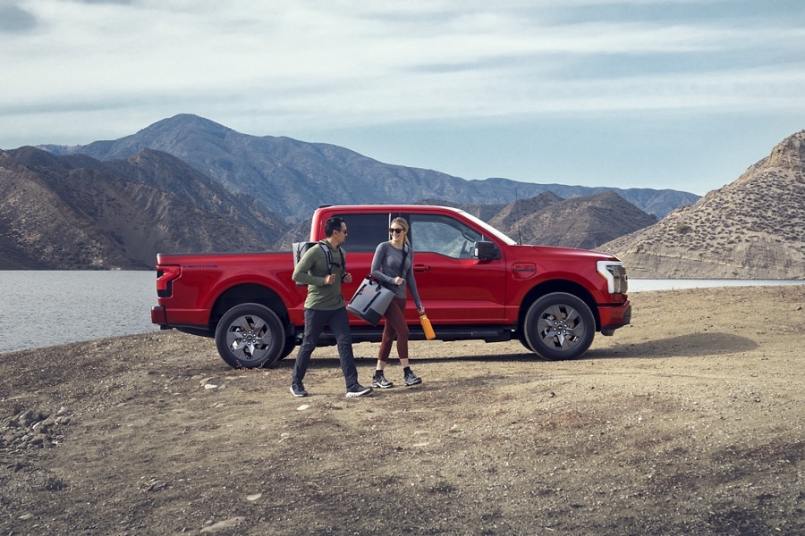 A couple walking near a 2023 Ford F-150® Lightning® parked near a lake with mountains in the background