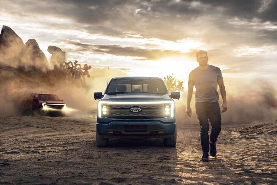 Lone guy walking through desert at dusk with two 2023 Ford F-150® Lightning® trucks running behind him