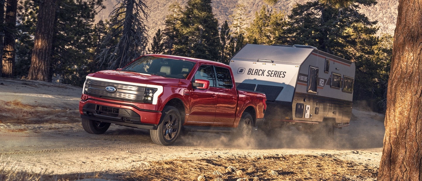 2023 Ford F-150® Lightning® pulling a camper on a dirt road through the woods