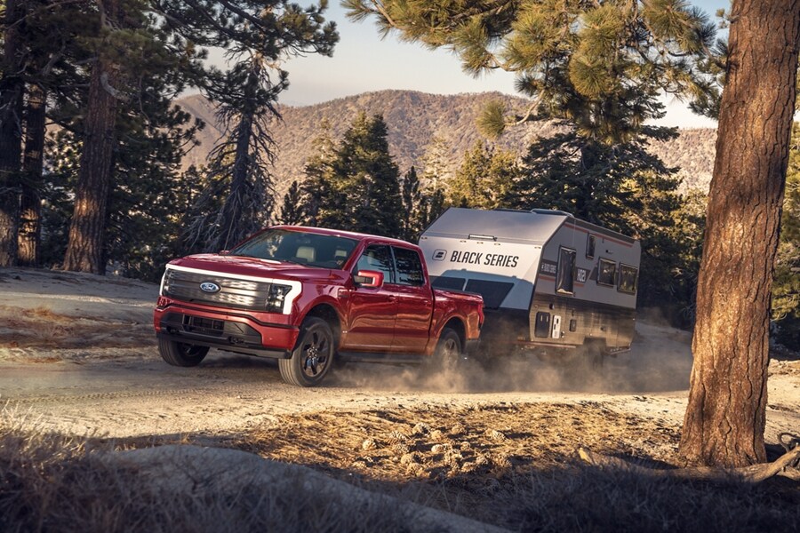 A 2023 Ford F-150® Lightning® towing a camper through a forest